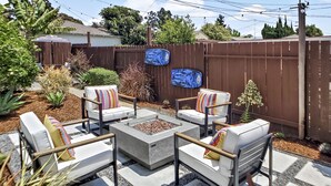 An outdoor patio area with four white chairs, a central fire pit, and a brown fence. - Close to Beach &  Major Attractions. Outdoor Patio with Firepit.  Free Parking. (Culver City)