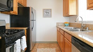 A compact kitchen with wooden cabinets, a stainless steel refrigerator, a black stove, and a granite countertop. - Close to Beach &  Major Attractions. Outdoor Patio with Firepit.  Free Parking. (Culver City)