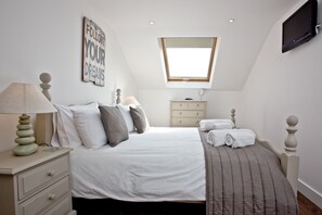 Ein Schlafzimmer mit Bett, Nachttisch, Lampe und einem an der Wand montierten Fernseher.