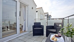 Ein Balkon mit zwei Korbstühlen, einem kleinen Tisch mit Brot und Weingläsern sowie einem Blumentopf.