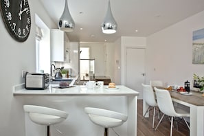 A modern kitchen with a central island, white bar stools, and pendant lighting.