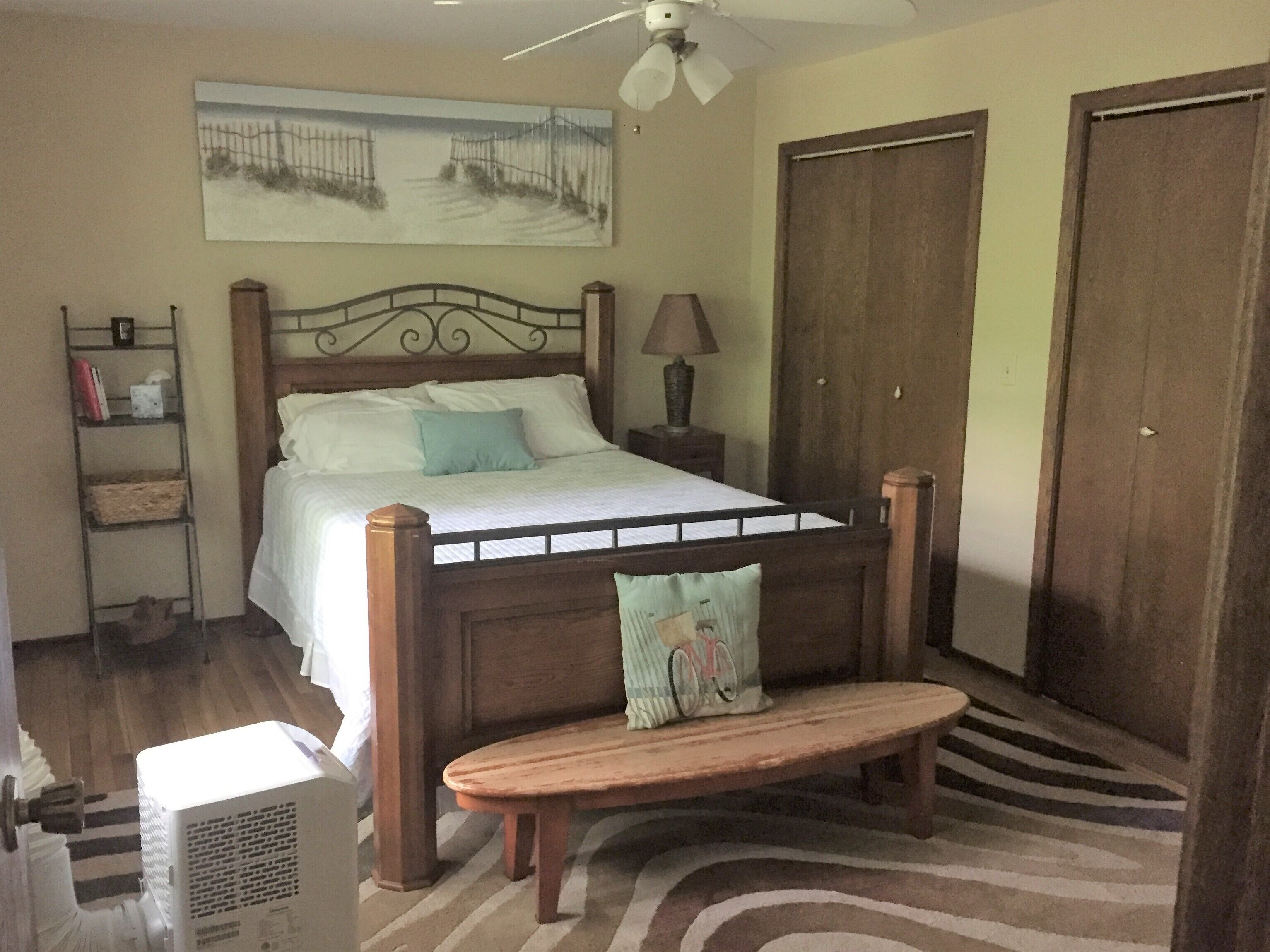 Un dormitorio con una cama, un banco, un calentador, una lámpara, un estante y un cuadro en la pared.