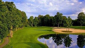 Un campo de golf con un estanque, árboles y cielo despejado.