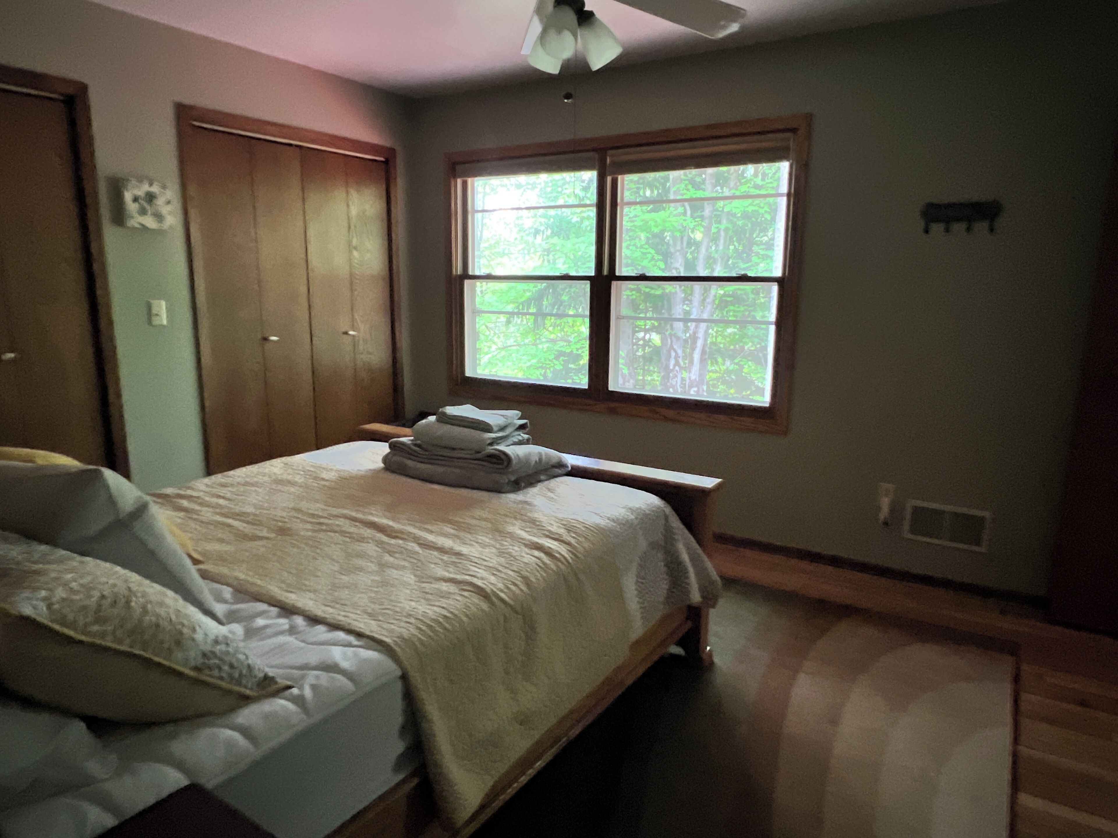 A bedroom with a bed, a window, a ceiling fan, and a door.