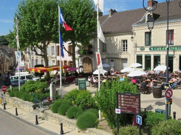 A café with outdoor seating, surrounded by greenery and a cobblestone street.