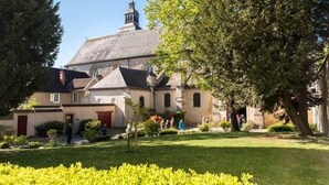 A historic building with a prominent tower and multiple smaller structures, surrounded by well-maintained gardens and trees.