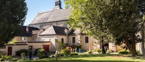 Un edificio histórico con una torre destacada y varias estructuras más pequeñas, rodeado de jardines y árboles bien cuidados.