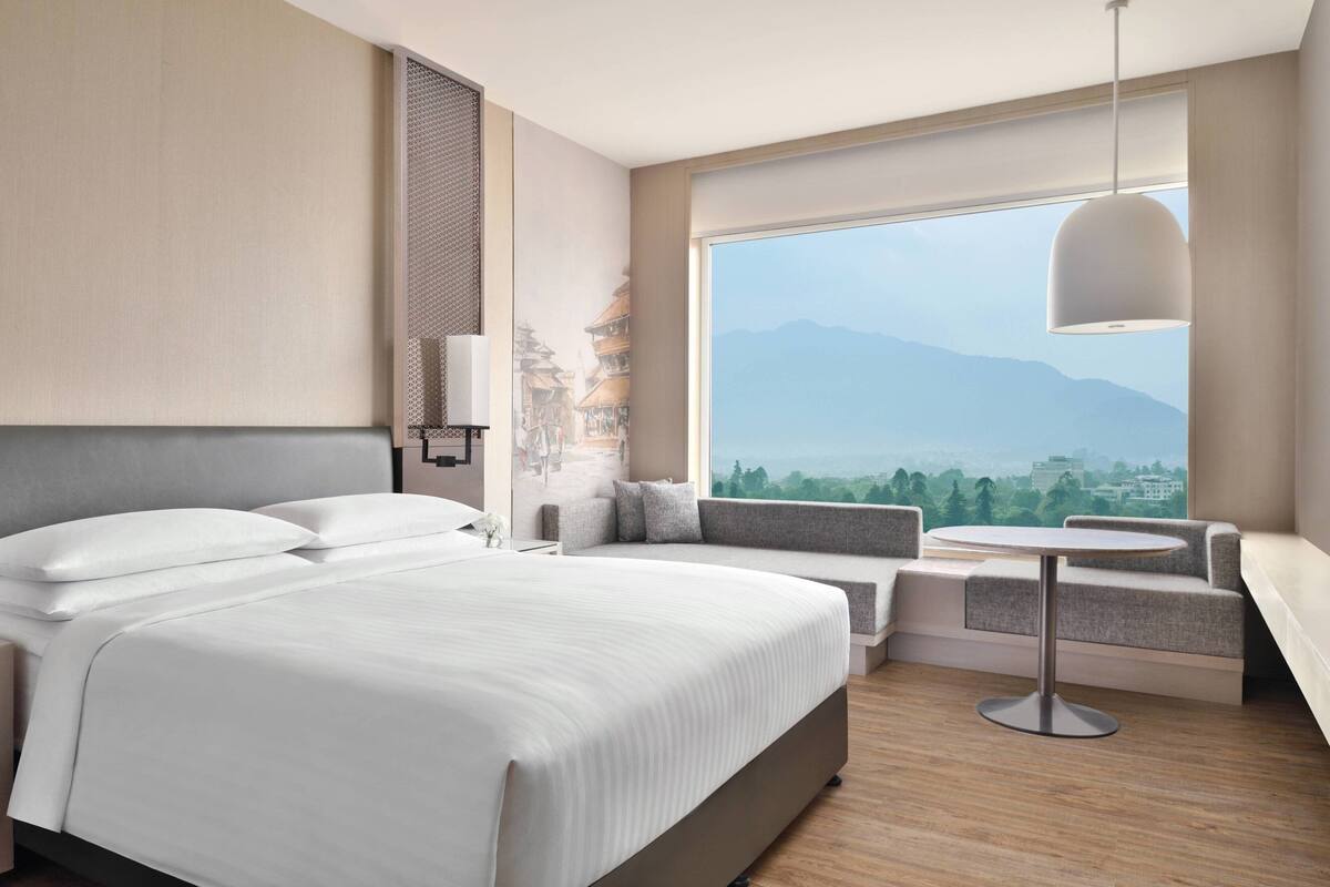 Ein modernes Hotelzimmer mit einem großen Bett, einer Sitzecke mit Bergblick und einem runden Tisch.