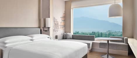 A modern hotel room with a large bed, a seating area with a view of mountains, and a round table.