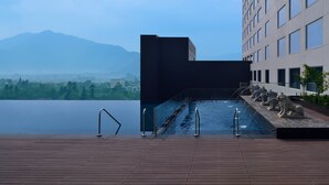 Una piscina en la azotea con vistas a montañas, un edificio moderno y estatuas de leones de piedra.