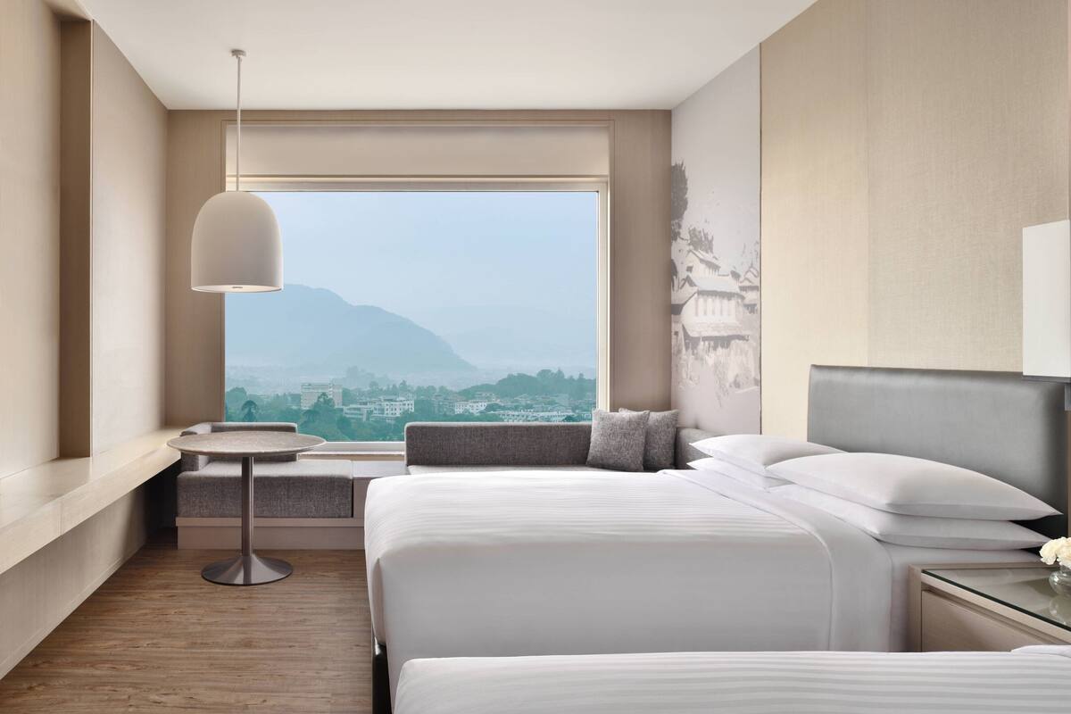 Ein Hotelzimmer mit großem Fenster, einem Bett, einem Nachttisch und einem runden Tisch.