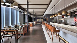 Un área de bar moderna con taburetes de madera, iluminación colgante y una barra larga.