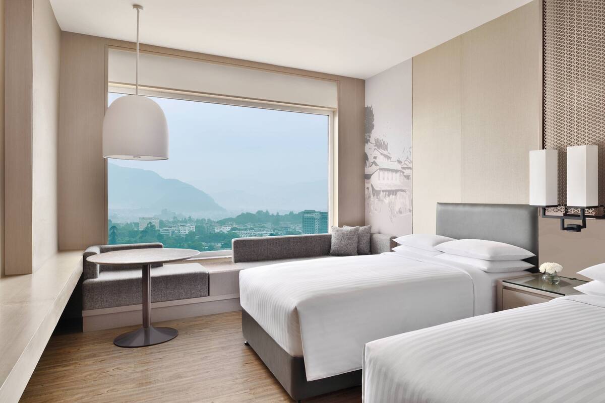 Ein Hotelzimmer mit großem Fenster, einem runden Tisch, zwei Betten und einer Sitzecke.