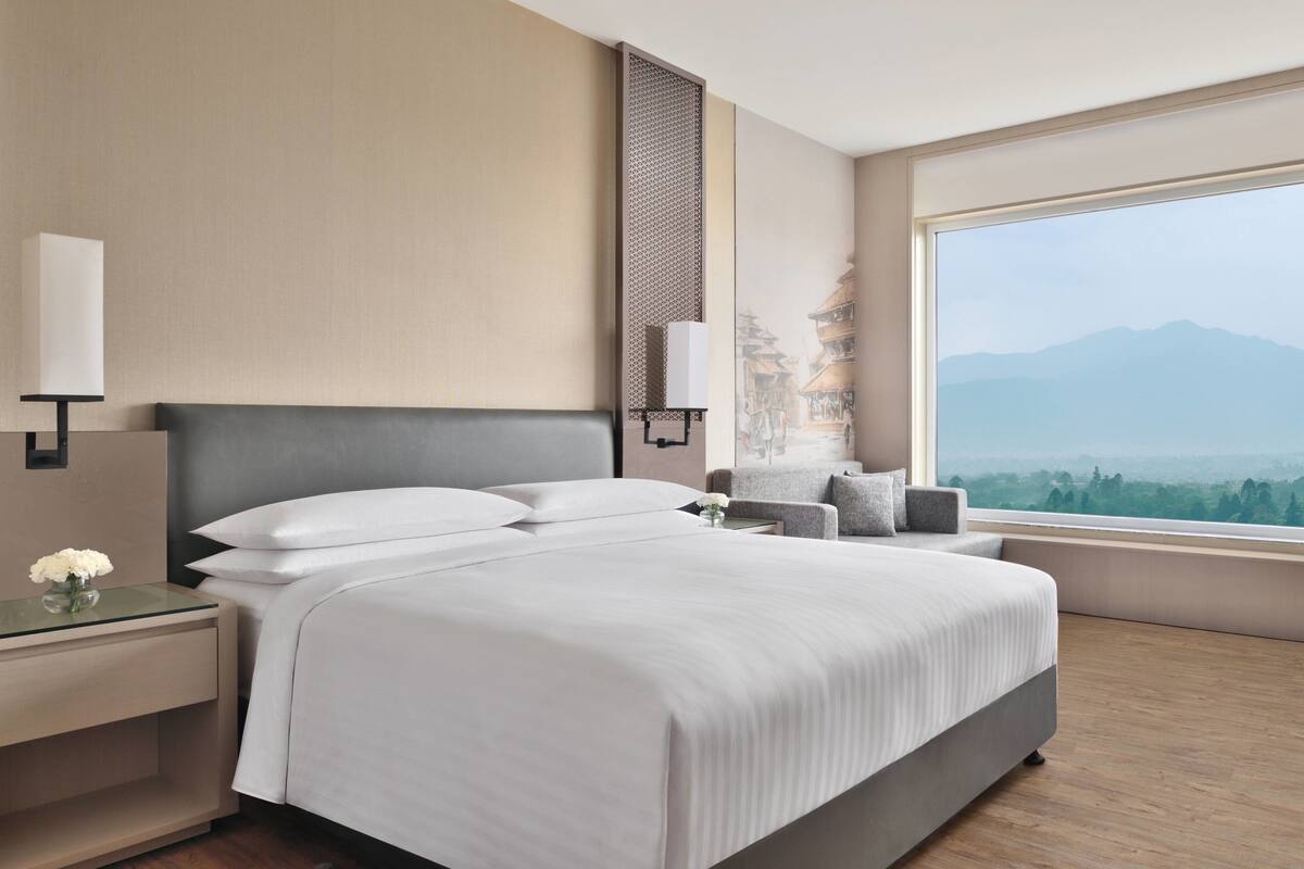 Ein modernes Hotelzimmer mit einem großen Bett, einem Nachttisch, einer Lampe und Bergblick durch das Fenster.