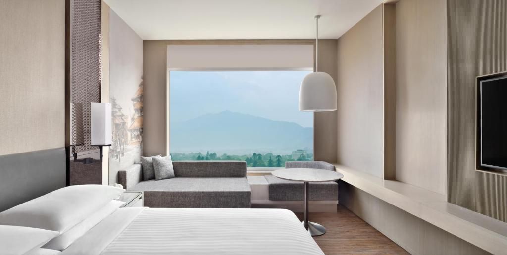A modern hotel room with a bed, seating area, and a TV.