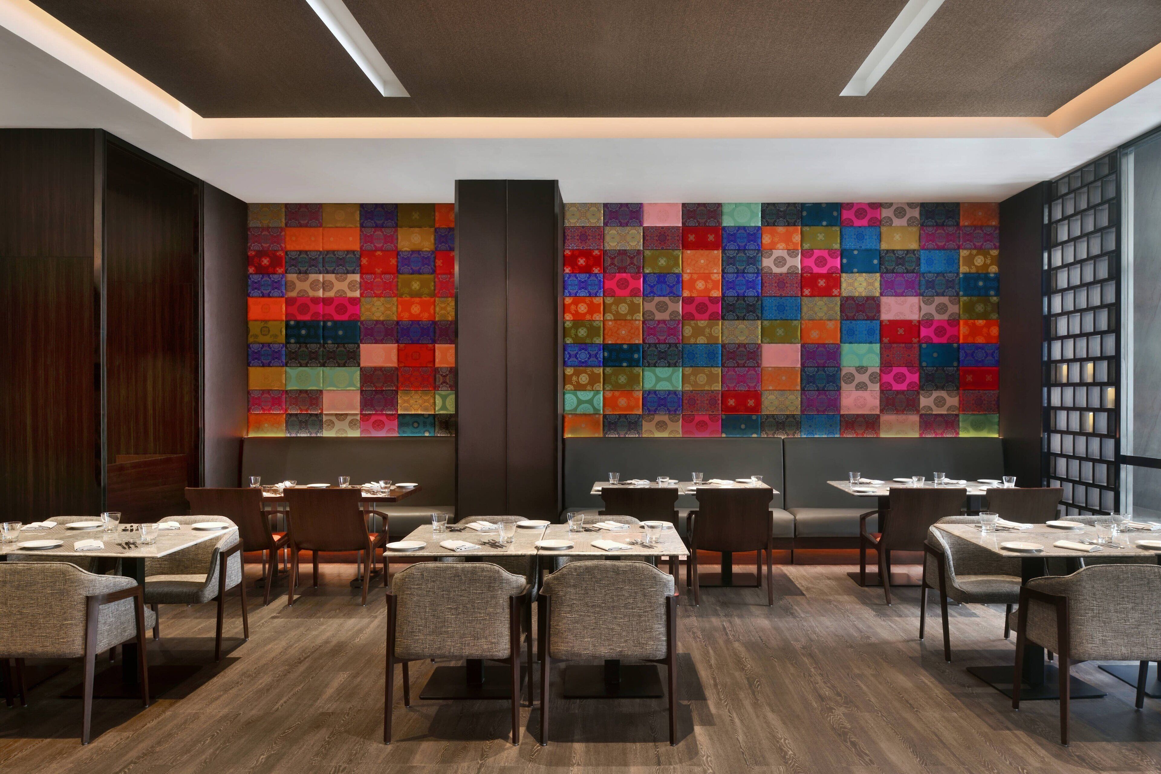 A restaurant with multiple tables and chairs, a colorful wall design, and a modern ceiling.