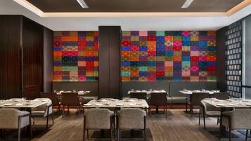 A restaurant with multiple tables and chairs, a colorful wall design, and a modern ceiling.