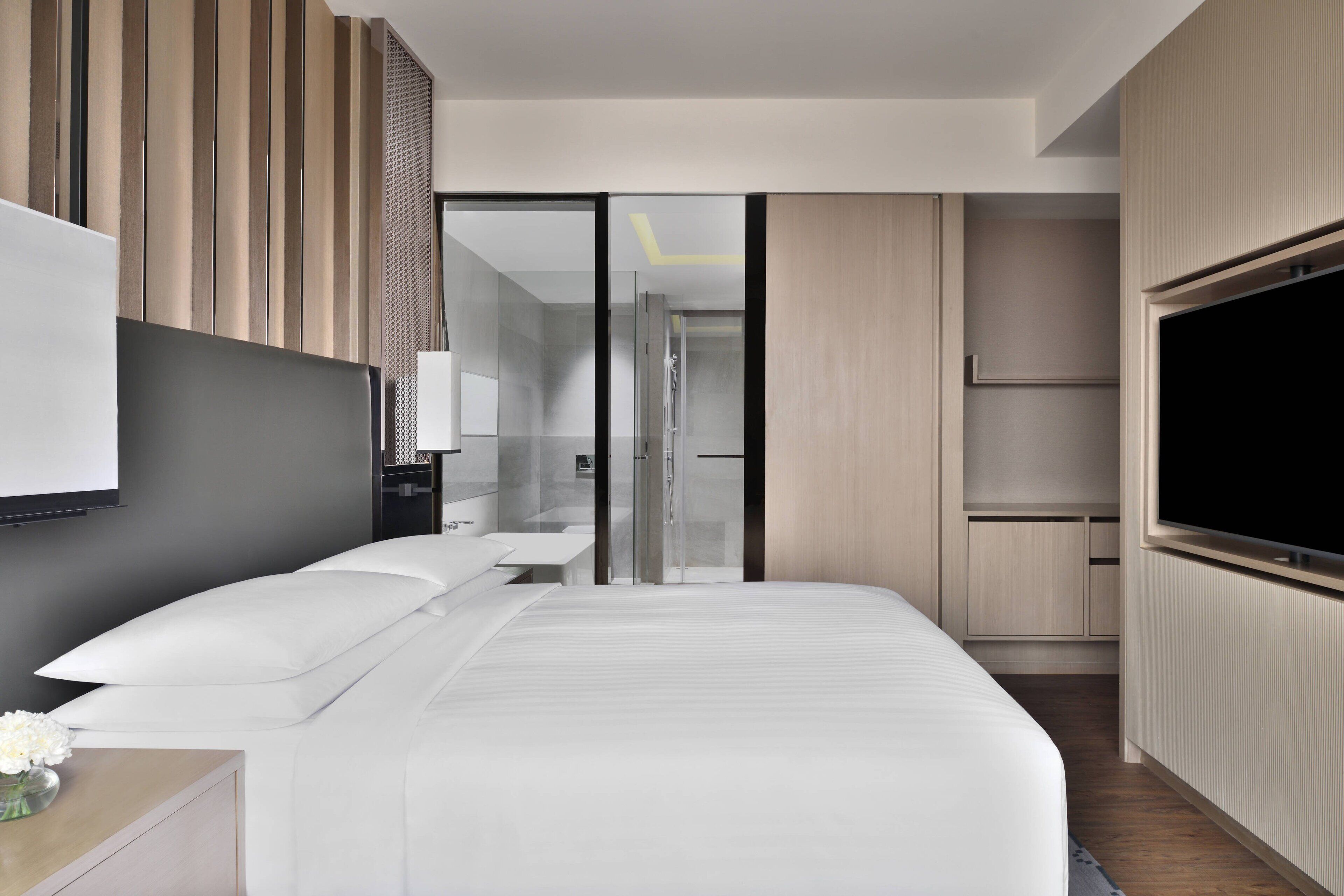 Una habitación de hotel moderna con una cama grande, televisor, escritorio con lámpara y vestidor.