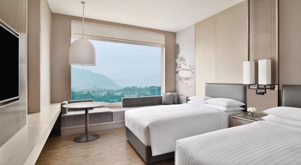 A hotel room with a large window, a bed, a bedside table, and a TV.
