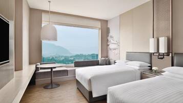 A hotel room with a large window, a bed, a bedside table, and a TV.