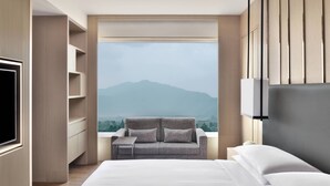 Una habitación de hotel moderna con una cama grande, un sofá, un televisor y una ventana con vista a la montaña.