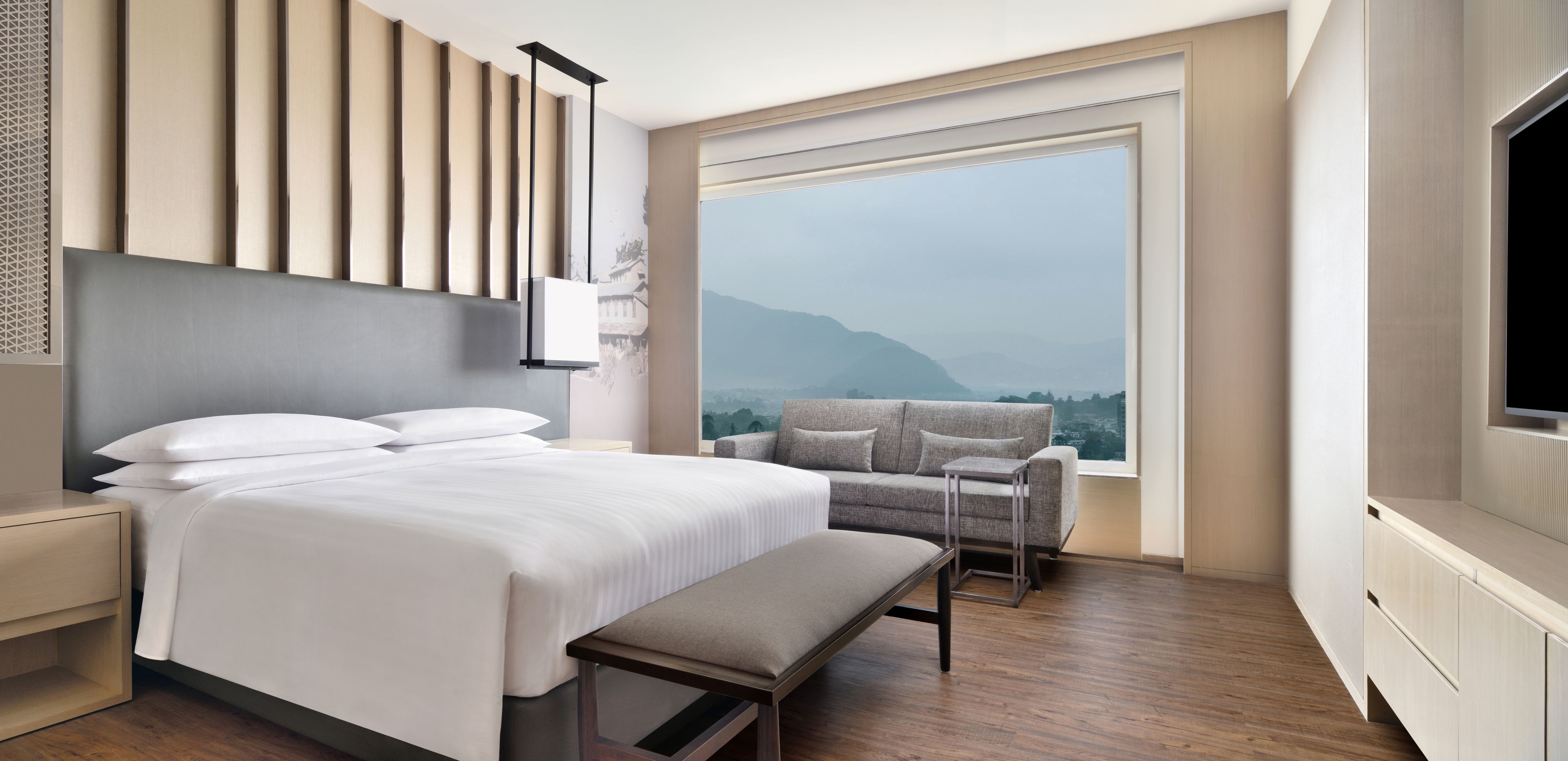 A modern hotel room with a large bed, a grey sofa, a small table, and a TV.