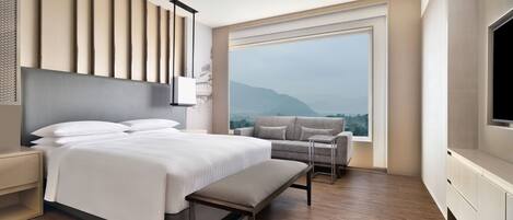 A modern hotel room with a large bed, a grey sofa, a small table, and a TV.