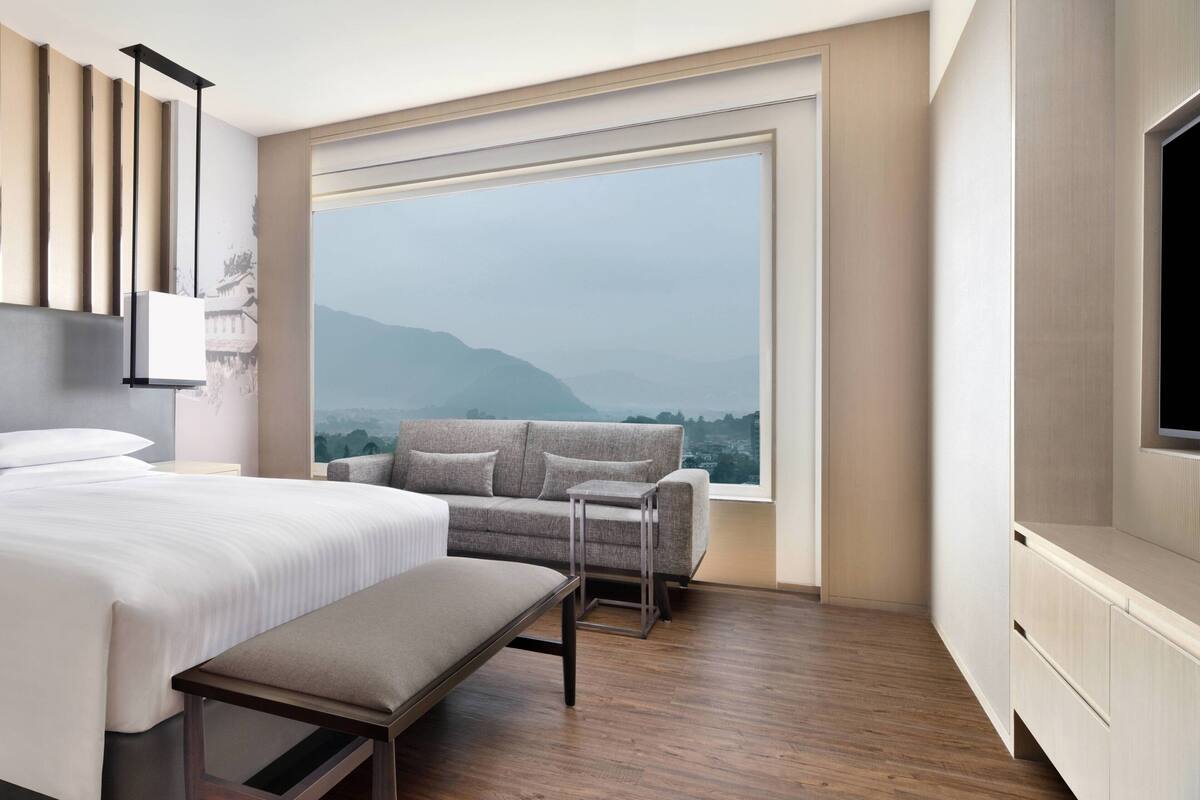 Ein modernes Hotelzimmer mit einem großen Bett, einer Couch, einer Bank und einem Fernseher.