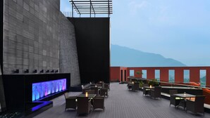 Un bar en la azotea con mesas al aire libre y una gran pantalla digital.