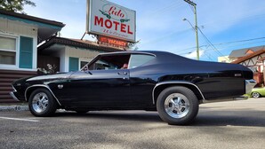 A classic black car parked in front of a motel with a sign that reads "Lido Motel Welcome". - Lido Motel (Radium Hot Springs)