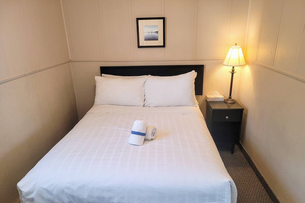 A hotel room with a neatly made bed, a bedside lamp, and a framed picture on the wall.