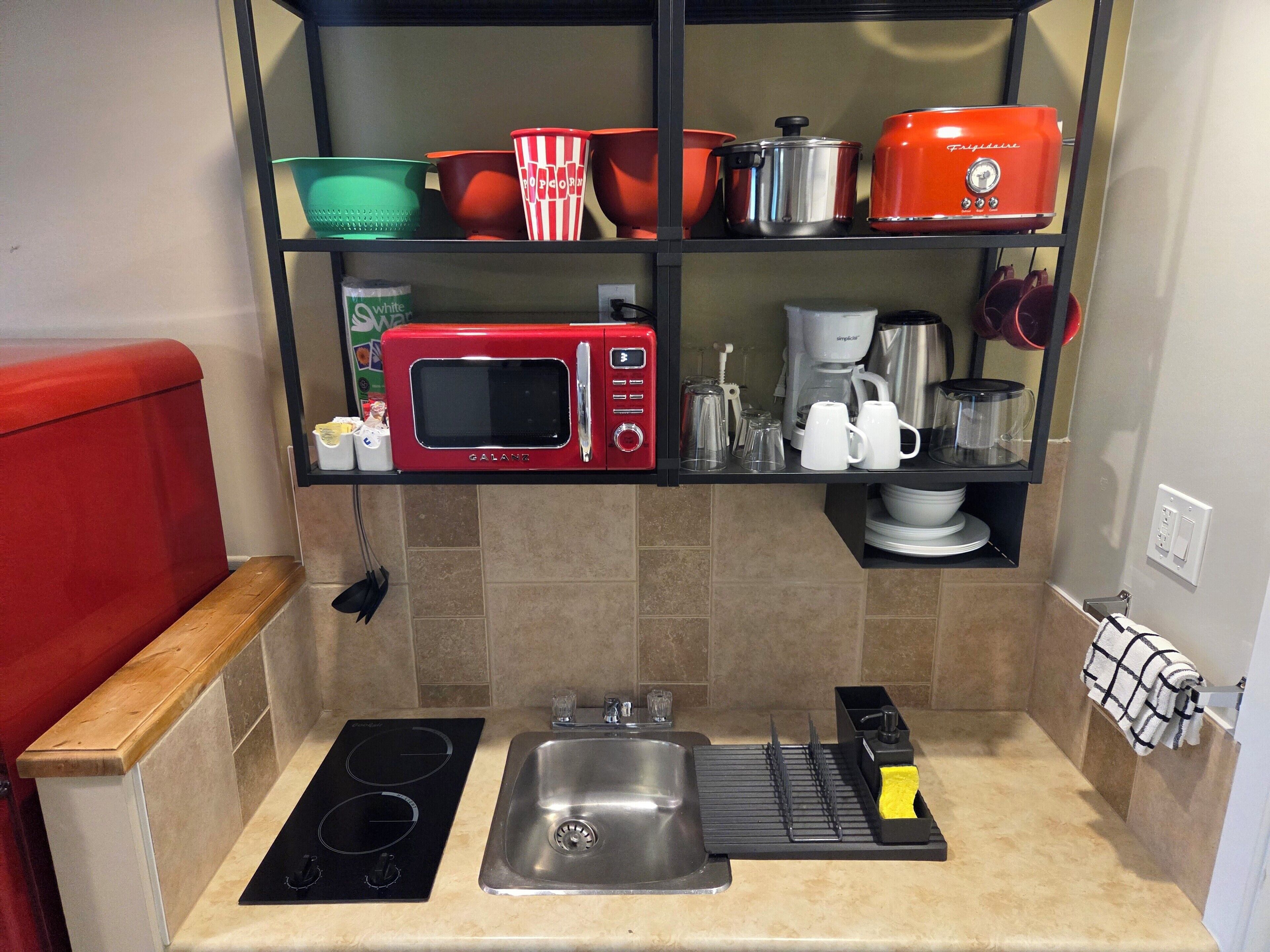 Una cocina compacta con microondas integrado, un lavamanos y una placa de cocina.