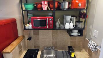 Una cocina compacta con microondas integrado, un lavamanos y una placa de cocina.
