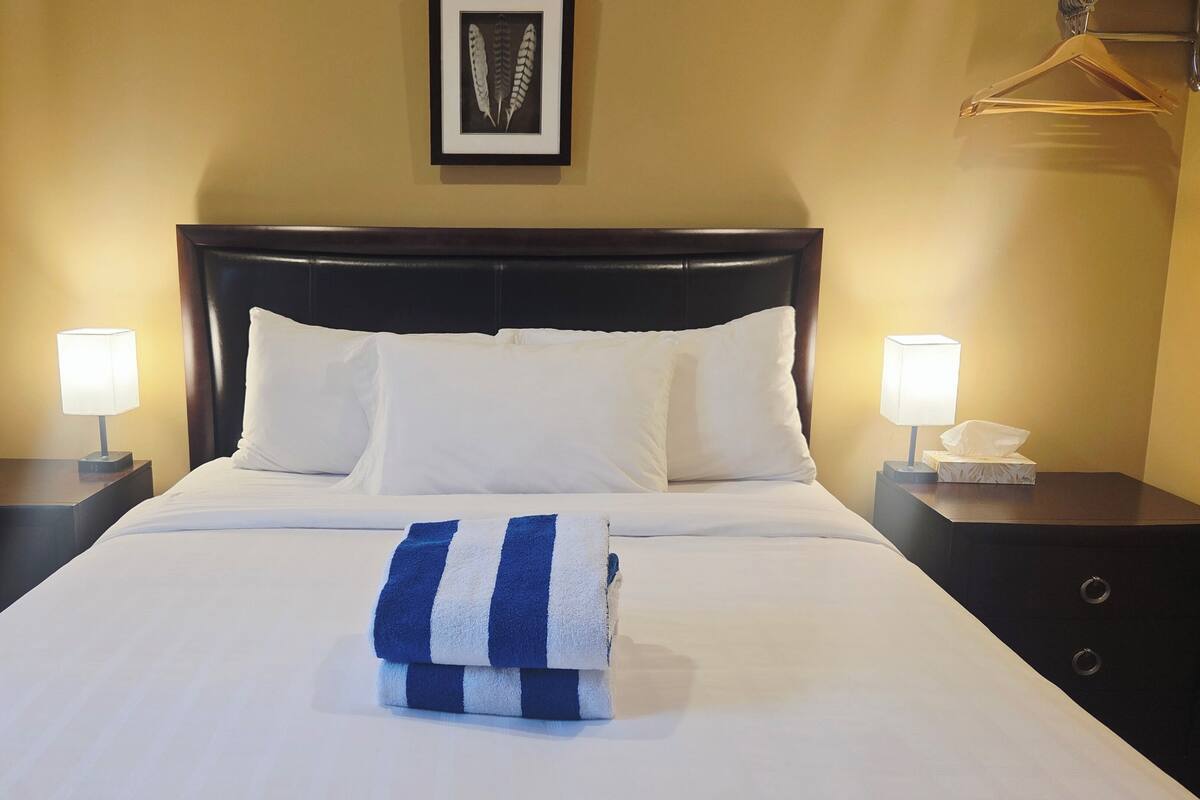 A hotel room with a bed, two bedside tables, a framed picture on the wall, and a towel on the bed.