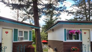 Two log cabin-style cabins with heart-shaped decorations, a tree in the foreground, and a red umbrella in the background. - Lido Motel (Radium Hot Springs)
