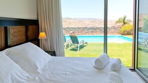 A hotel room with a large bed, a view of a swimming pool, and a grassy area with chairs. - Salobre Golf Villas - Holiday Rental Par 4 - 8 (San Bartolomé de Tirajana)