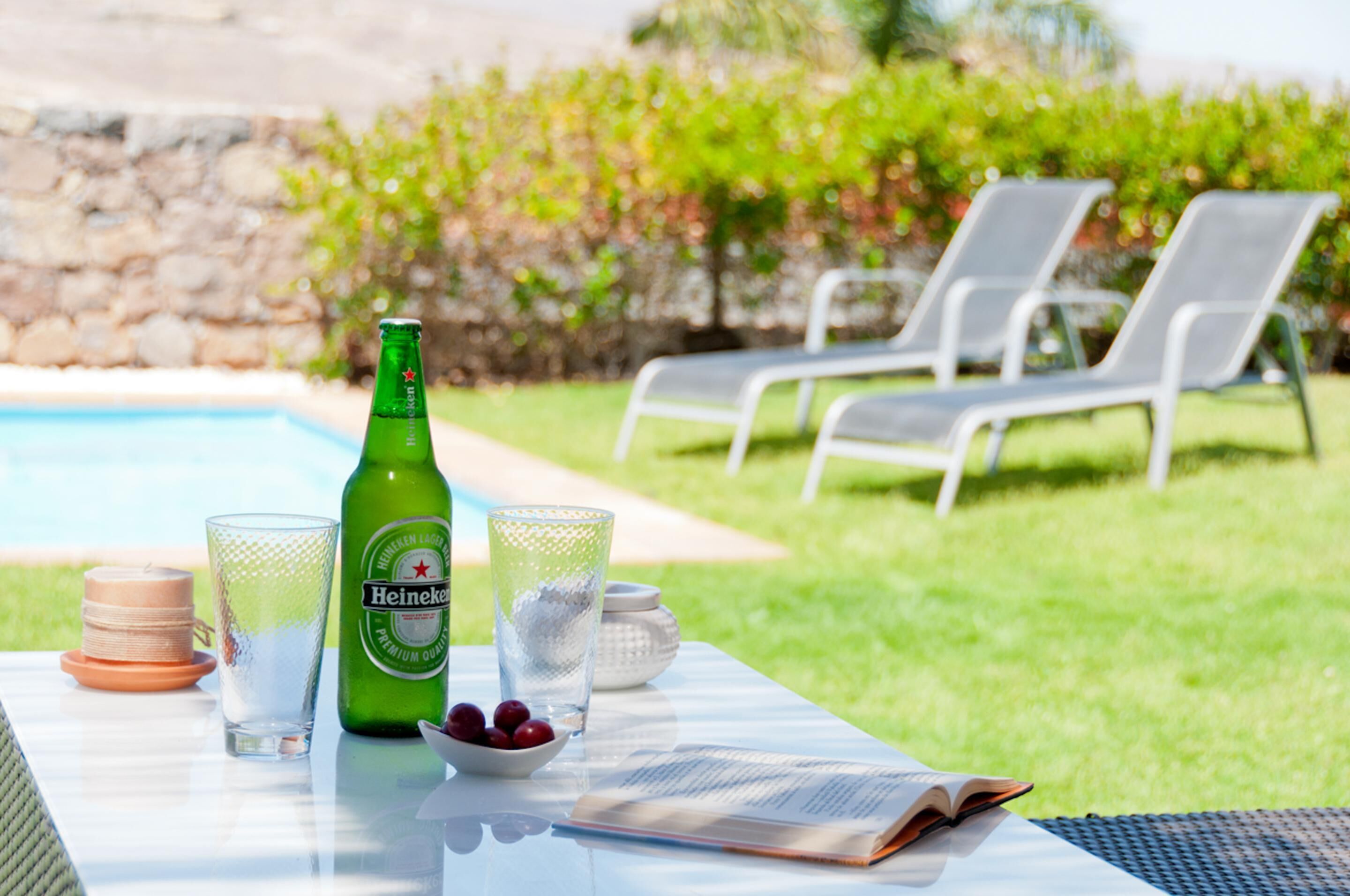 A table with a bottle of Heineken, glasses, a bowl of cherries, and a menu.