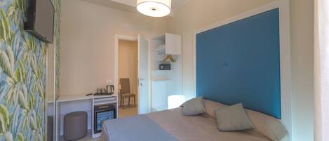 A bedroom with a bed, a desk, a chair, and a small refrigerator.