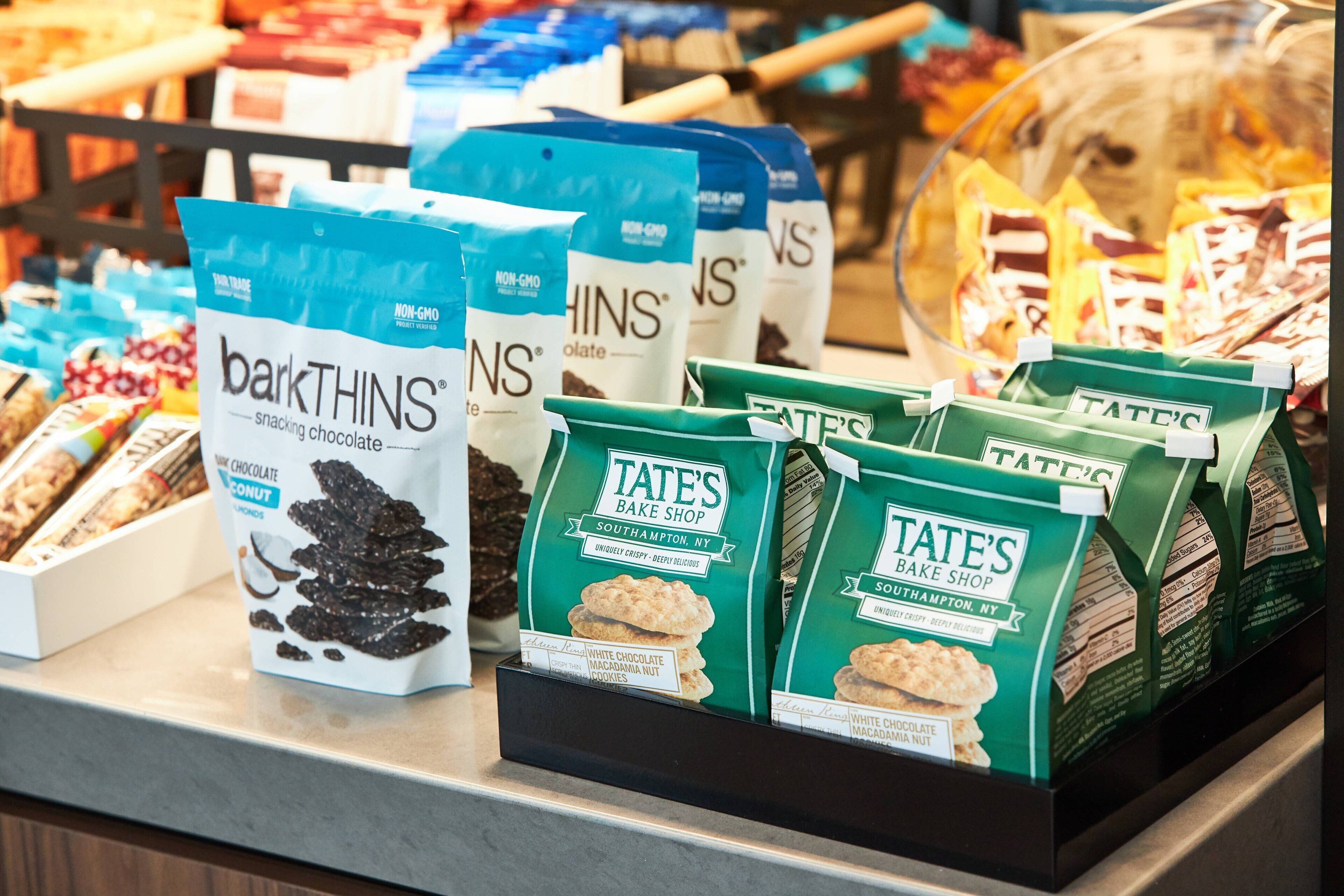 A display of snack bags, including 'barkTHINS' and 'TATE'S Bake Shop' products.