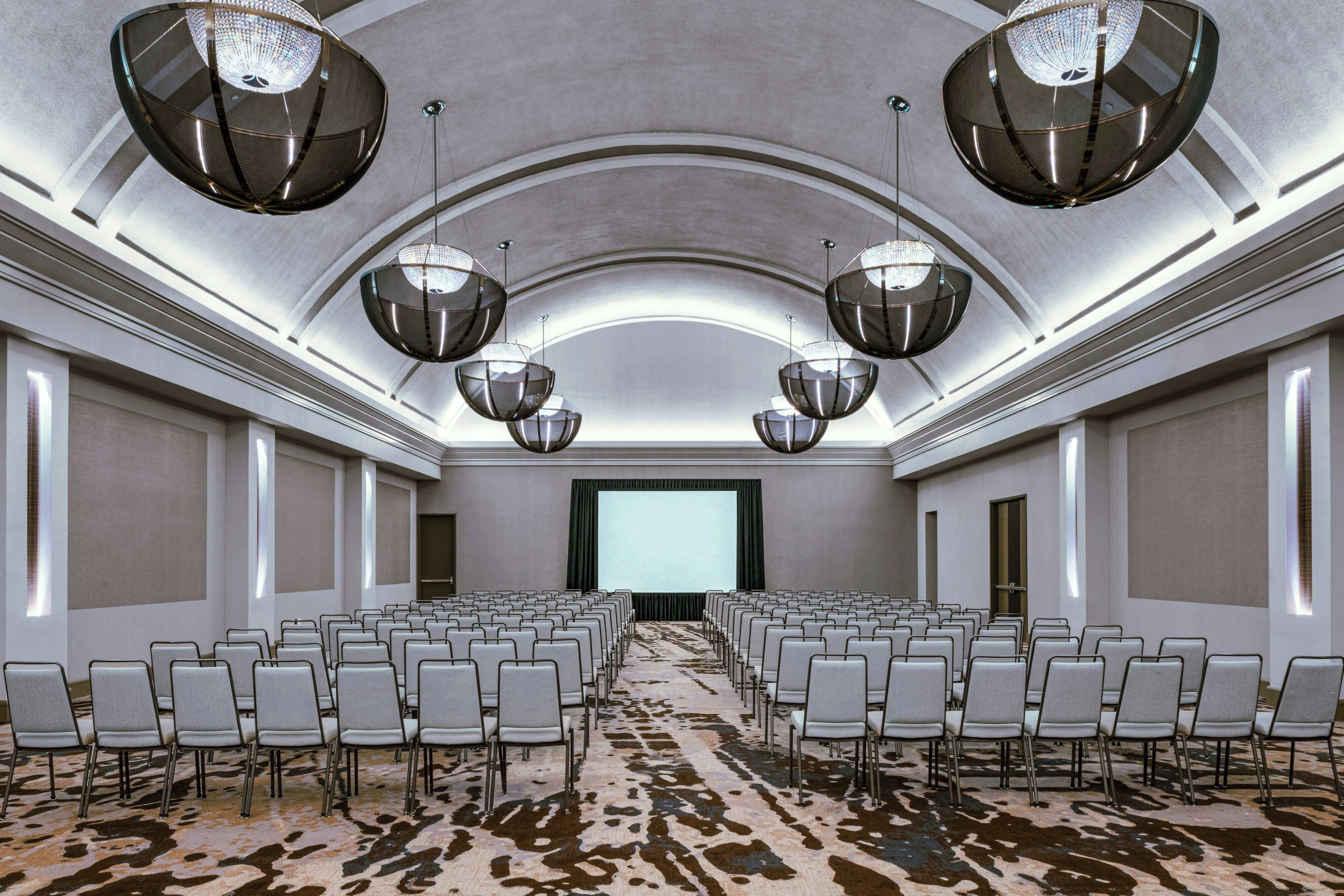 A conference room with rows of chairs, a large screen, and multiple chandeliers.