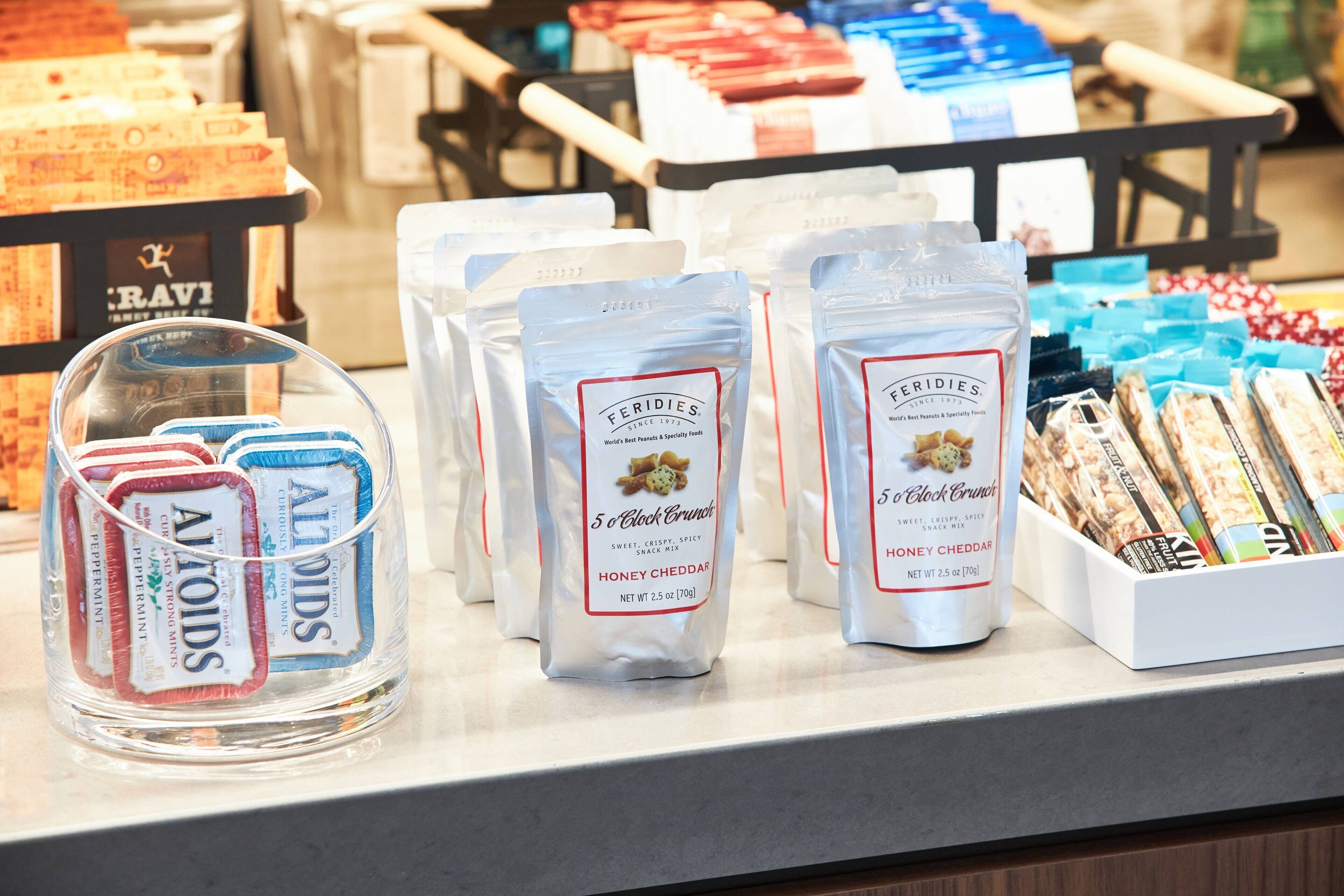 A display of snack mix bags and a container of almonds on a store counter.