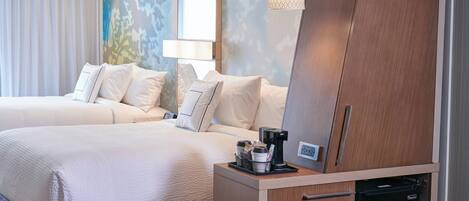 A hotel room with two beds, a coffee maker, a mini-fridge, and a wall-mounted lamp.