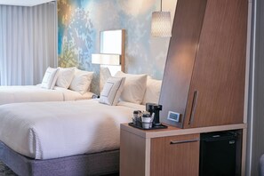 Habitación de hotel con dos camas, cafetera, mini refrigerador y lámpara de pared.