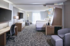 A hotel room with a bed, a desk with a chair, a television, a lamp, and a small kitchenette. - Courtyard by Marriott Jackson (Jackson)