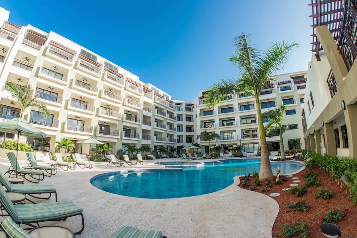 A hotel with a swimming pool, multiple balconies, and lounge chairs.