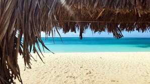 A beach with a thatched roof structure, clear turquoise water, and sandy shore. - Aruba Stop Vacation Rentals (Noord)