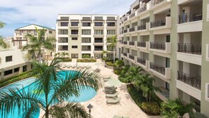 A hotel with multiple floors, a central courtyard with a swimming pool, and surrounding greenery. - Aruba Stop Vacation Rentals (Noord)