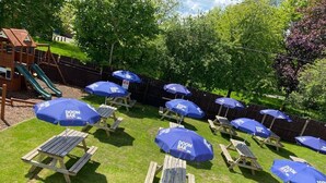A backyard with picnic tables and blue umbrellas labeled "DOOM BAR". - Alcester Inn (Alcester)