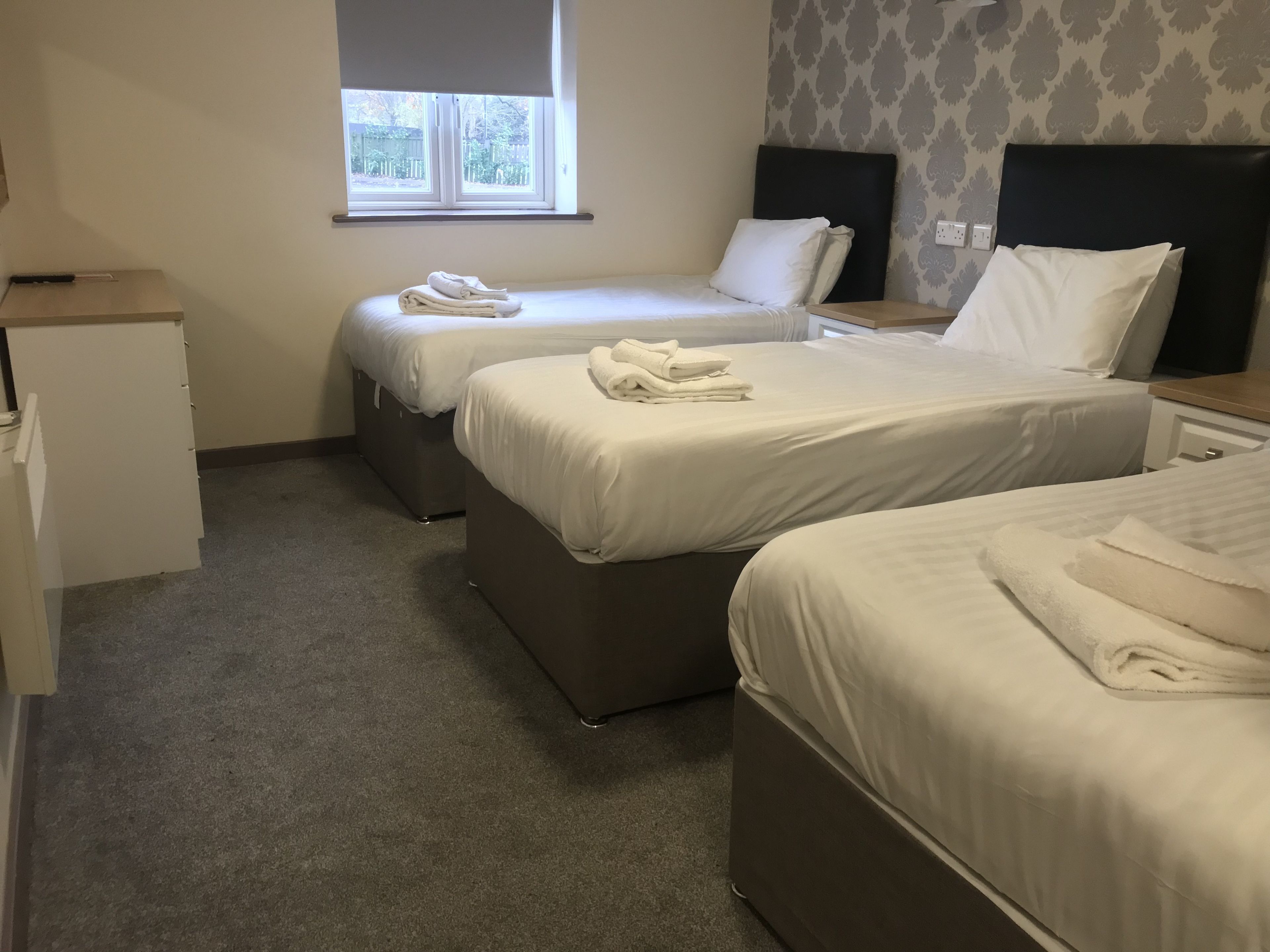 Hotelkamer met drie bedden, een klein bureau en een raam met uitzicht.