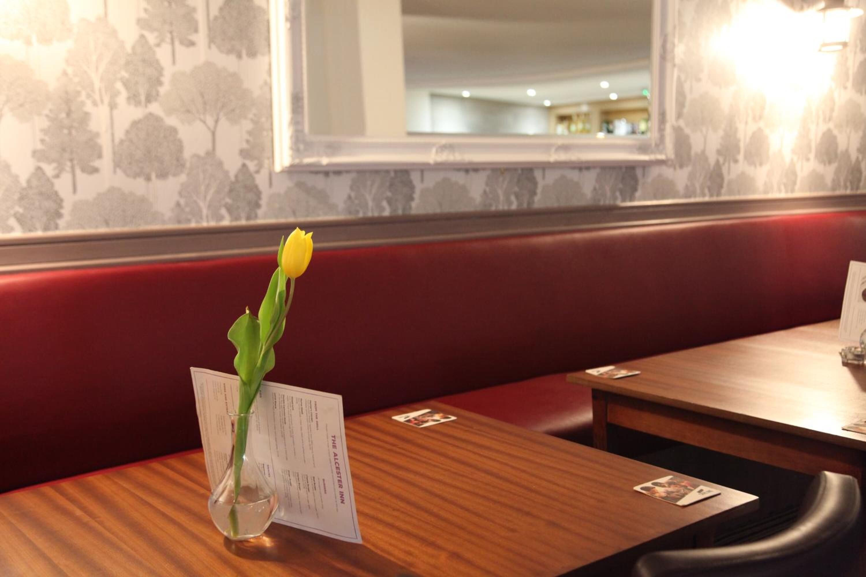 A restaurant interior with a wooden table, a menu, and a vase with a single yellow flower.